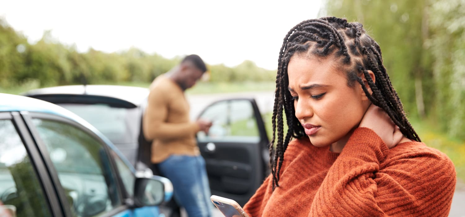 A female driver holding her forehead while sitting behind the wheel of her car as if experiencing whiplash.