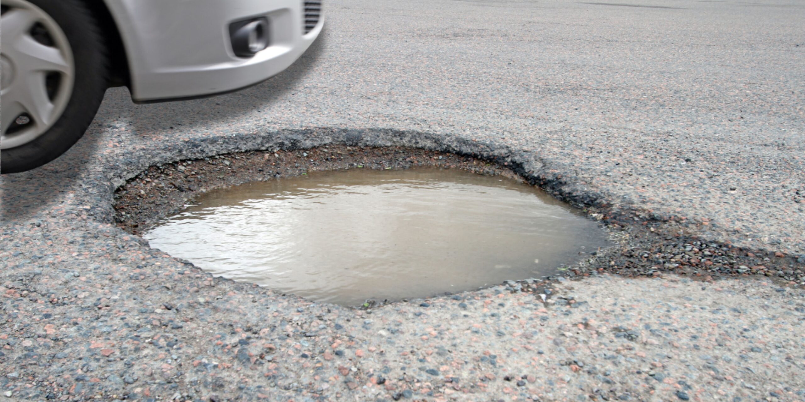 Vehicle hitting a deep pothole filled with water on a Cleveland roadway, highlighting how pothole impacts can cause jolts that lead to back, neck, and spinal strain.