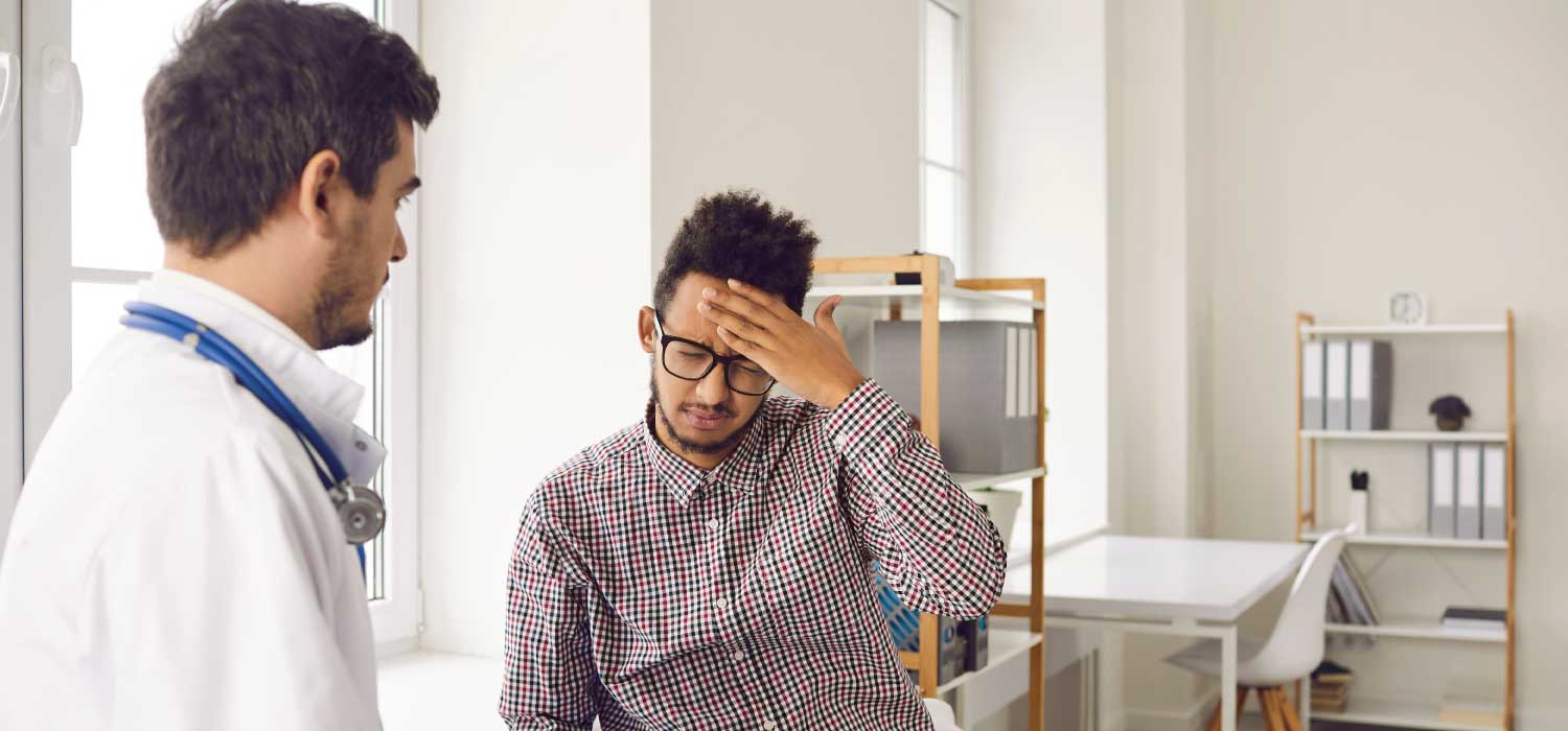A male patient with a medical provider holding his head as if he has a headache.